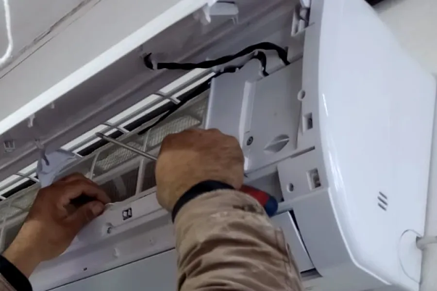 Trabajo real en obra: manos trabajando en una unidad interior de aire acondicionado con la tapa abierta.