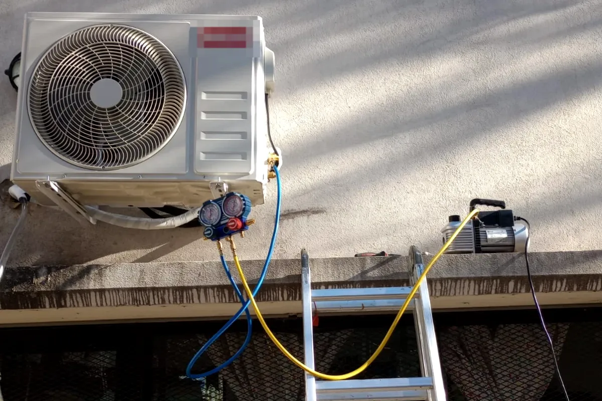 Trabajo real en obra: unidad exterior de aire acondicionado recién instalada, con manómetros y bomba de vacío conectados.