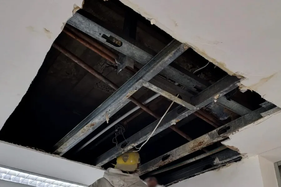 Trabajo real en obra: cielorraso abierto con la estructura de perfiles a la vista, mientras una persona trabaja desde una escalera.