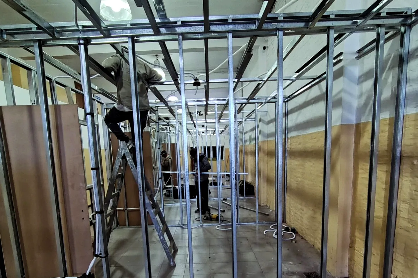 Trabajo real en obra: estructura de perfiles de drywall para dividir un salón en oficinas, con dos personas trabajando.