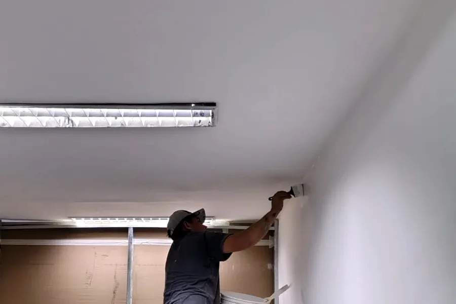 Trabajo real en obra: persona pintando sobre una escalera una oficina armada con drywall.